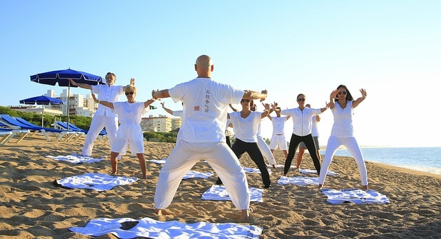 A group of people practicing yoga on a sandy beach, engaging in various poses while facing the instructor. This form of yoga enhances muscle strength, flexibility, and mental focus, which are beneficial for runners to prevent injuries and improve overall performance.